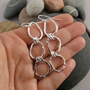 Coast Trio Drop Earrings: hammer textured free form sterling silver long statement earrings displayed on a hand by Mikel Grant Jewellery