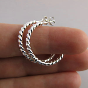 Twisted sterling silver open hoop studs displayed on a hand by Mikel Grant Jewellery. Modern, comfortable, artisan made.
