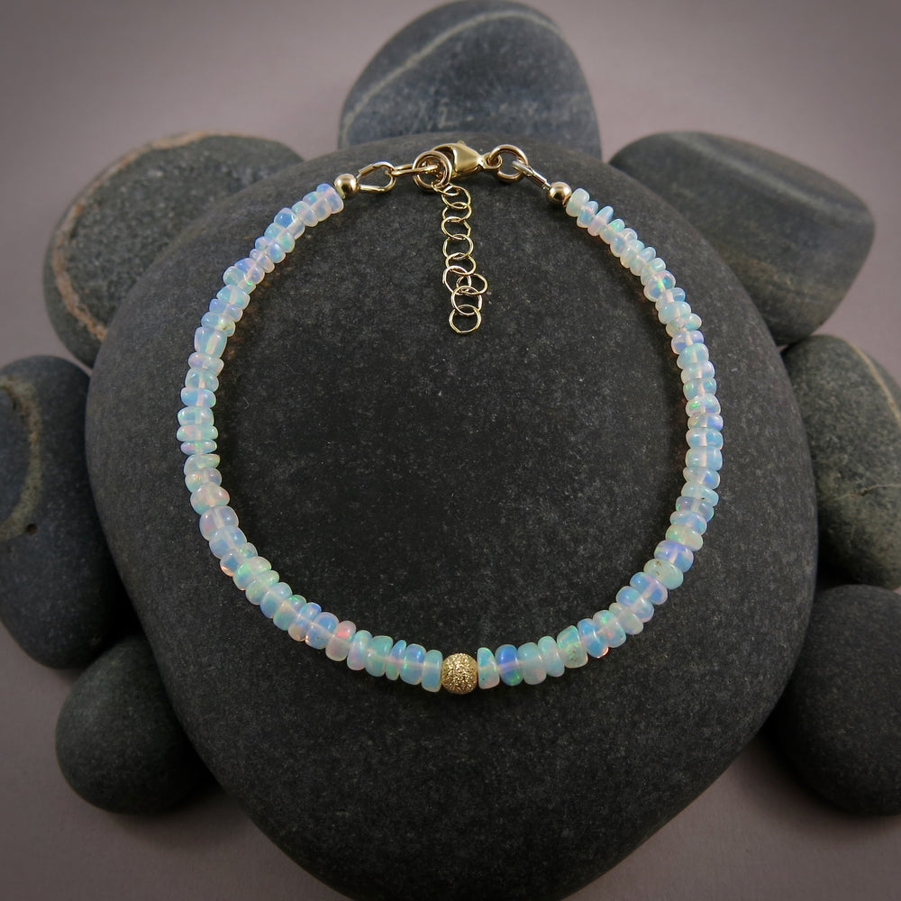 A Welo opal bead bracelet is displayed on a black beach rock.  The gems display lovely rainbow colours in a gently graduating size.