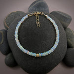 A Welo opal bead bracelet is displayed on a black beach rock.  The gems display lovely rainbow colours in a gently graduating size.