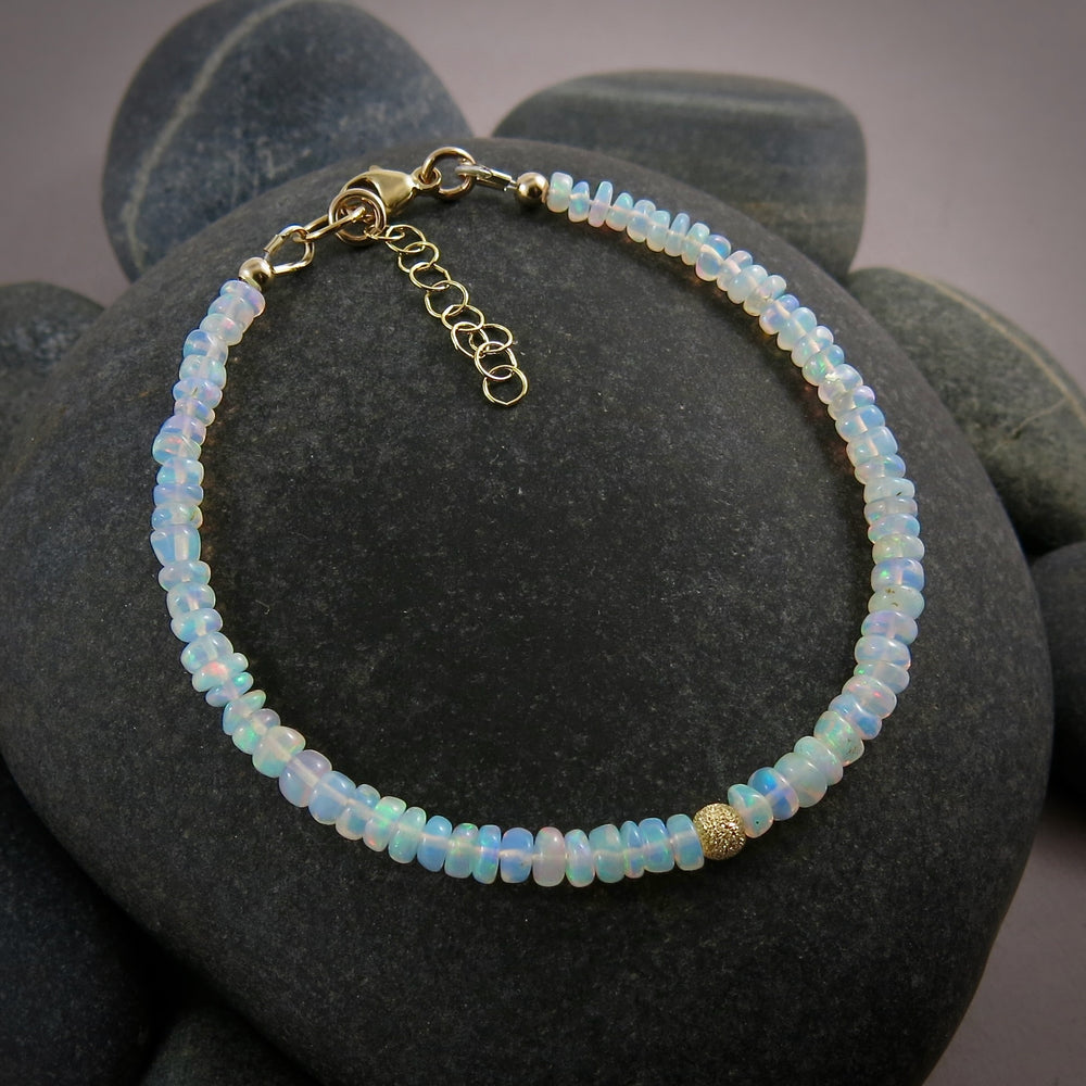 A Welo opal bead bracelet is displayed on a black beach rock.  The gems display lovely rainbow colours in a gently graduating size.