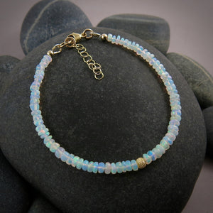 A Welo opal bead bracelet is displayed on a black beach rock.  The gems display lovely rainbow colours in a gently graduating size.