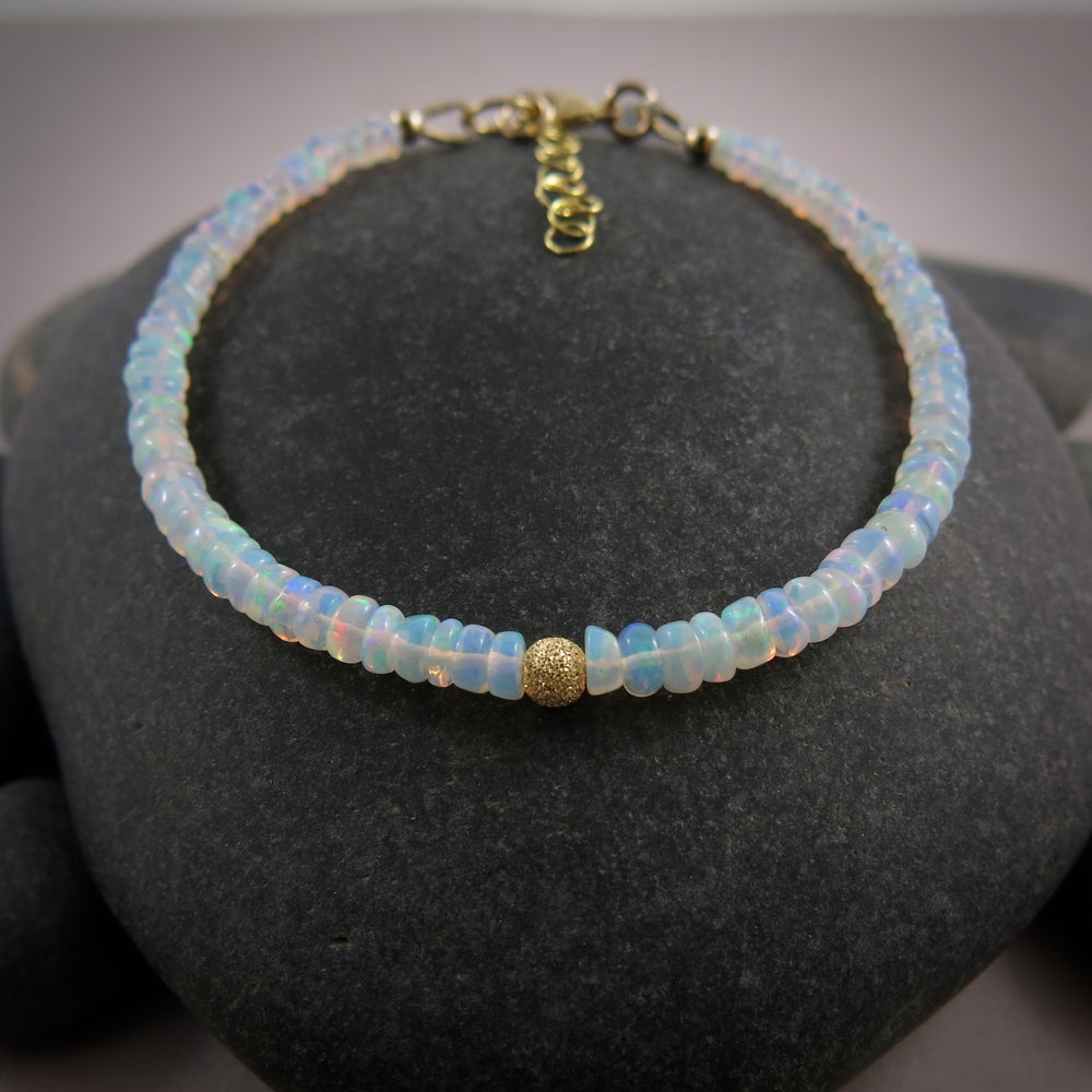 A Welo opal bead bracelet is displayed on a black beach rock.  The gems display lovely rainbow colours in a gently graduating size.