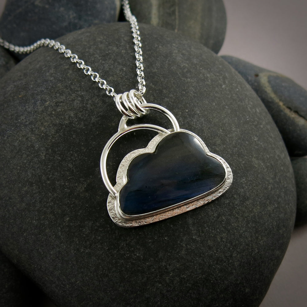 A "Silver Linings" necklace by Mikel Grant Jewellery.  An electric blue labradorite gemstone in the shape of a cloud is bezel set in sterling silver on a silver back.  A "silver lining" of silver surrounds the stone and a single silver "rainbow" sits above the cloud.