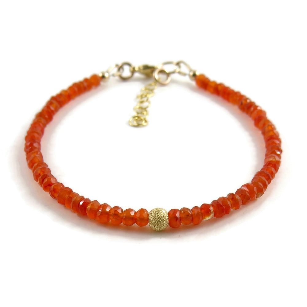 A bright orange gemstone bead bracelet is displayed on a white background.  The carnelian beads are faceted and sparkly and the bracelet features a gold filled sparkly bead in the centre as well as a gold filled clasp, ring and adjustable chain.