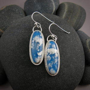 Daydream earrings by Mikel Grant Jewellery.  A pair of slender oval plume agate doublets set in subtly textured sterling silver.  The plume agates display fluffy white clouds against a vibrant blue background reminiscent of the sky.