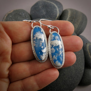 Daydream earrings by Mikel Grant Jewellery.  A pair of slender oval plume agate doublets set in subtly textured sterling silver.  The plume agates display fluffy white clouds against a vibrant blue background reminiscent of the sky.