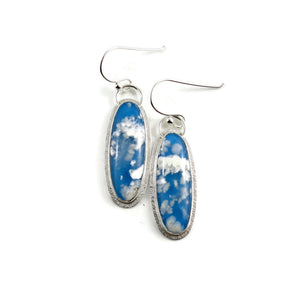 Daydream earrings by Mikel Grant Jewellery.  A pair of slender oval plume agate doublets set in subtly textured sterling silver.  The plume agates display fluffy white clouds against a vibrant blue background reminiscent of the sky.