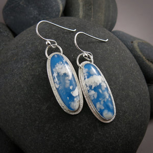 Daydream earrings by Mikel Grant Jewellery.  A pair of slender oval plume agate doublets set in subtly textured sterling silver.  The plume agates display fluffy white clouds against a vibrant blue background reminiscent of the sky.