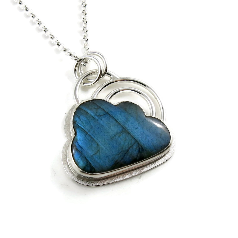 A sterling silver necklace by Mikel Grant Jewellery.  Featuring an electric blue labradorite gemstone in the shape of a cloud.   The labradorite is bezel set in silver with a silver "lining" frame around the outside and a double "rainbow" above the cloud made from two silver curved rings.