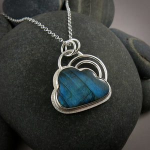 A sterling silver necklace by Mikel Grant Jewellery.  Featuring an electric blue labradorite gemstone in the shape of a cloud.   The labradorite is bezel set in silver with a silver "lining" frame around the outside and a double "rainbow" above the cloud made from two silver curved rings.