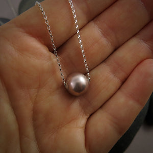 A pearl necklace is displayed on a hand.  The round, lilac-pink pearl is suspended on a sterling silver rolo chain that slides through the centre of the pearl.