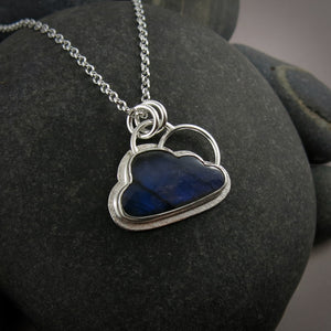 A "Silver Linings" necklace by Mikel Grant Jewellery.  A cloud shaped electric blue labradorite gemstone is bezel set on a silver background.  A silver "lining" is visible all the way around the necklace and  a single silver "rainbow" sits above the cloud.  