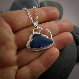 A "Silver Linings" necklace by Mikel Grant Jewellery.  A cloud shaped electric blue labradorite gemstone is bezel set on a silver background.  A silver "lining" is visible all the way around the necklace and  a single silver "rainbow" sits above the cloud.  