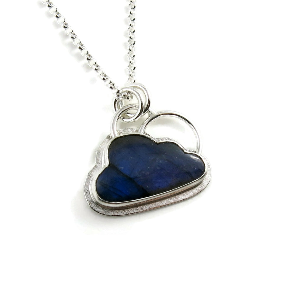 A "Silver Linings" necklace by Mikel Grant Jewellery.  A cloud shaped electric blue labradorite gemstone is bezel set on a silver background.  A silver "lining" is visible all the way around the necklace and  a single silver "rainbow" sits above the cloud.  