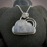 A handcrafted sterling silver necklace by Mikel Grant Jewellery.  A rainbow moonstone shaped like a cloud is set in sterling silver with a "silver lining" of silver surrounding the gem.  A double "rainbow" of curved silver wire rests atop the cloud.  