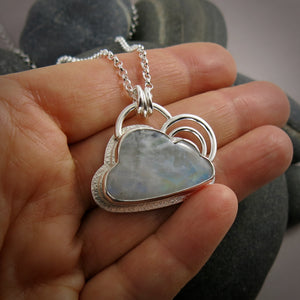 A sterling silver necklace featuring a cloud shaped rainbow moonstone.  The cloud is bezel set and has a silver "lining" around the outside and two silver curved pieces above the cloud resembling a rainbow.  