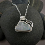 A sterling silver necklace featuring a cloud shaped rainbow moonstone.  The cloud is bezel set and has a silver "lining" around the outside and two silver curved pieces above the cloud resembling a rainbow.  