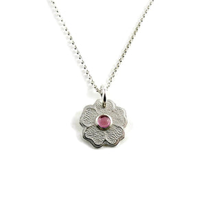 Silver necklace with a floral pendant featuring a pink gemstone on a white background