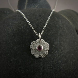 Silver necklace with a floral pendant featuring a pink gemstone on a dark gray surface.
