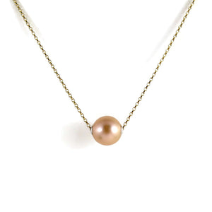 A pearl necklace is displayed on a white background.  The round, peachy-pink pearl is suspended on a yellow gold filled rolo chain that slides through the centre of the pearl.