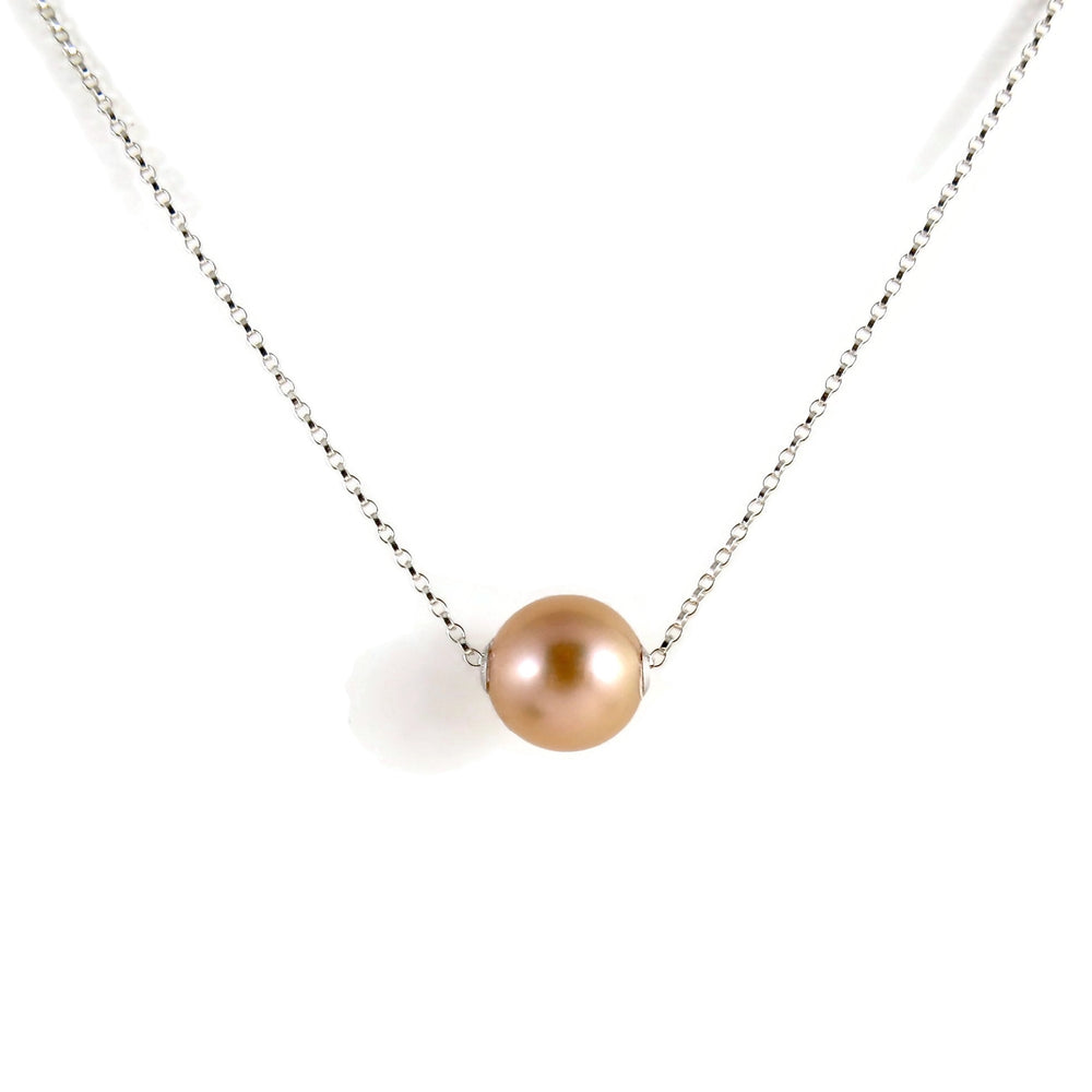 A pearl necklace is displayed on a white background.  The round, peachy-pink pearl is suspended on a sterling silver rolo chain that slides through the centre of the pearl.