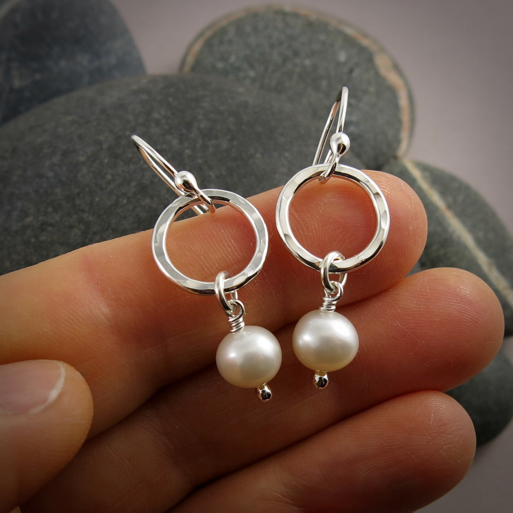 Silver earrings with pearl drops held between fingers against a stone background
