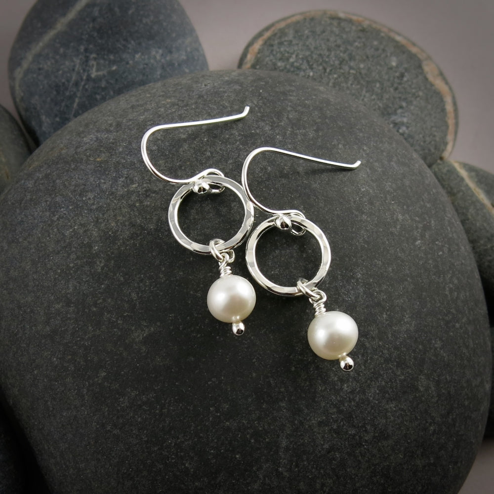 Silver earrings with pearl drops on a dark stone surface.