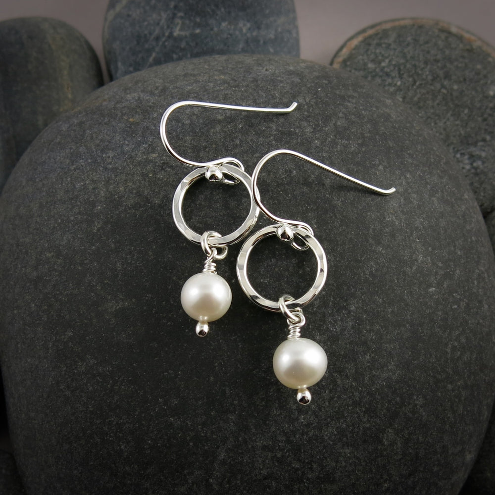 Silver earrings with pearl drops on a dark stone surface