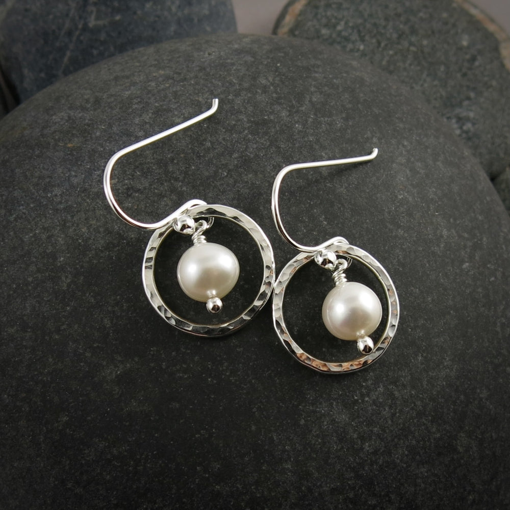 Silver earrings with pearl drops on a dark stone surface