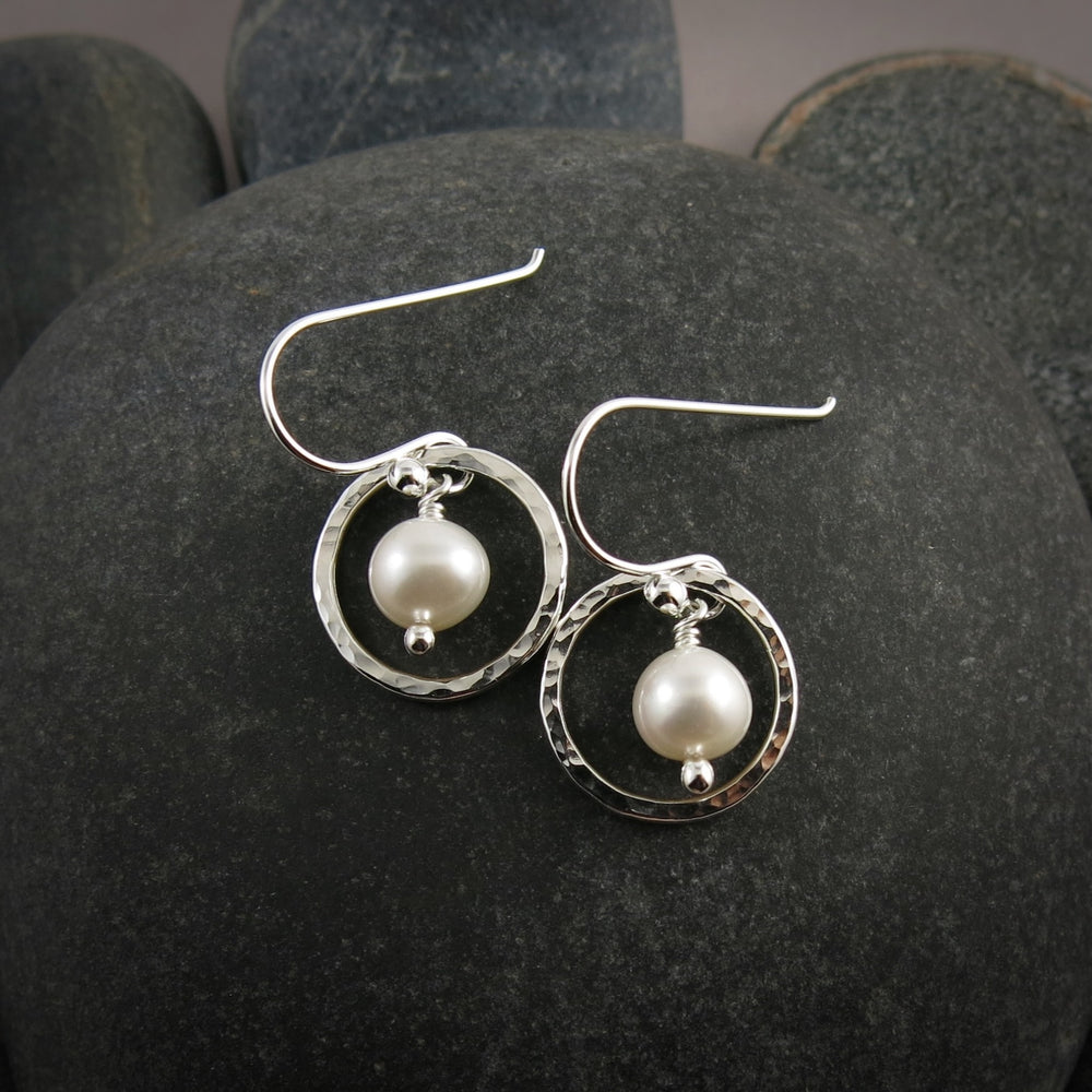 Silver earrings with nesting pearl drops on a dark stone surface.