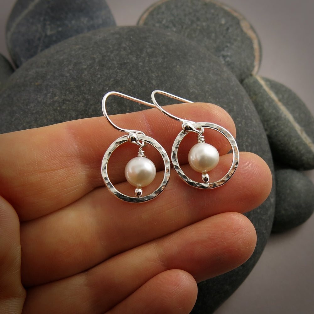 Silver earrings with pearl drops held between fingers against a stone background