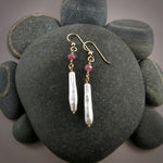 A pair of gemstone & pearl earrings are displayed on a black beach rock.  The earrings feature a faceted pink sapphire bead atop lustrous white stick pearls.  The ear wires and headpins are 14K gold filled.
