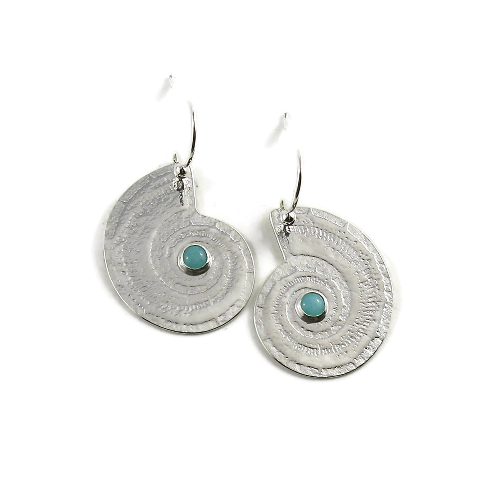 A pair of silver earrings are displayed on a white background.  The earrings feature an impression of an ammonite and a little seafoam green amazonite gemstone in the middle of their centre swirls.