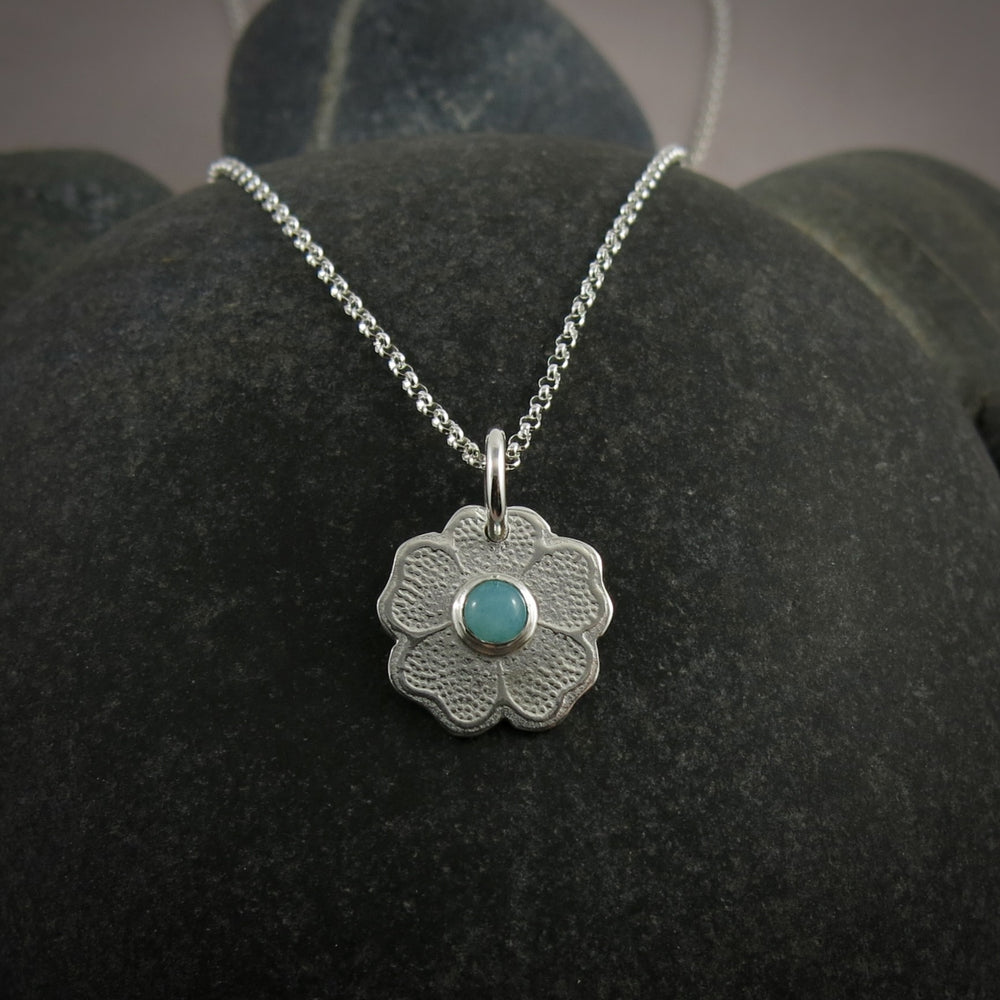 Silver necklace with a floral pendant featuring a seafoam green amazonite gemstone on a black beach rock.
