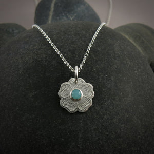 Silver necklace with a floral pendant featuring a seafoam green amazonite gemstone on a black beach rock.