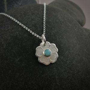 Silver necklace with a floral pendant featuring a seafoam green amazonite gemstone on a black beach rock.
