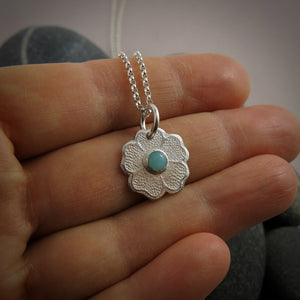 Silver necklace with a floral pendant featuring a seafoam green amazonite gemstone on a hand.