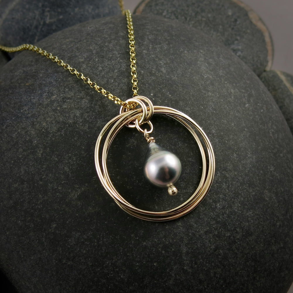 10K Gold Knot Pendant with a Silver Tahitian Pearl Drop in the Centre.  Displayed against a black beach rock.