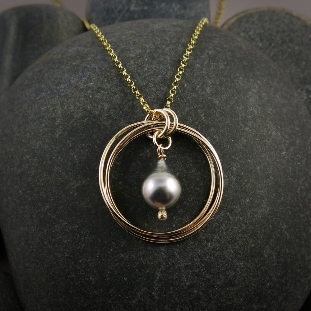 10K Gold Knot Pendant with a Silver Tahitian Pearl Drop in the Centre.  Displayed against a black beach rock.
