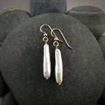 A pair of pearl earrings are displayed on a black beach rock.  The rectangular white stick pearls hang from gold filled ear wires.