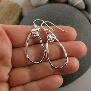 Classic Coast Earrings: west coast beach inspired free form sterling silver dangles with rustic hammer texture displayed on a hand by Mikel Grant Jewellery