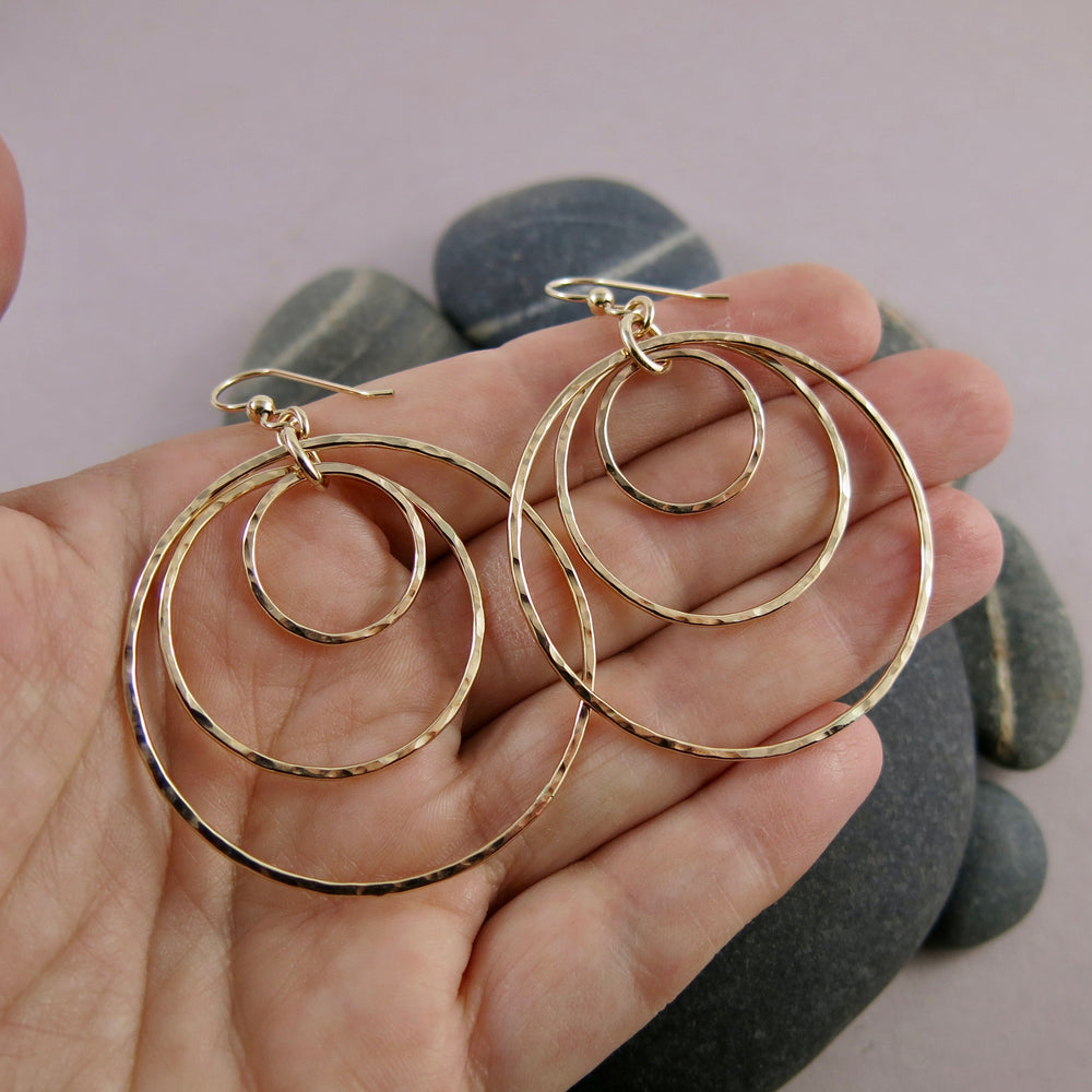 Hammered gold nesting trio circle earrings by Mikel Grant Jewellery. Artisan made bold dangle earrings.  Shown displayed on a hand.