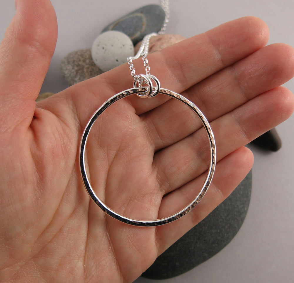 Artisan made open circle necklace in thick, hammer textured sterling silver with a long 30" silver rolo chain by Mikel Grant Jewellery.  Seen here displayed on a hand.