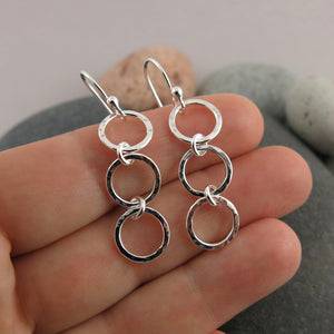 Breathe Trio Drop Earrings: hammer textured sterling silver open circle trio drop earrings displayed on a hand by Mikel Grant Jewellery. Artisan made on the Sunshine Coast of BC.