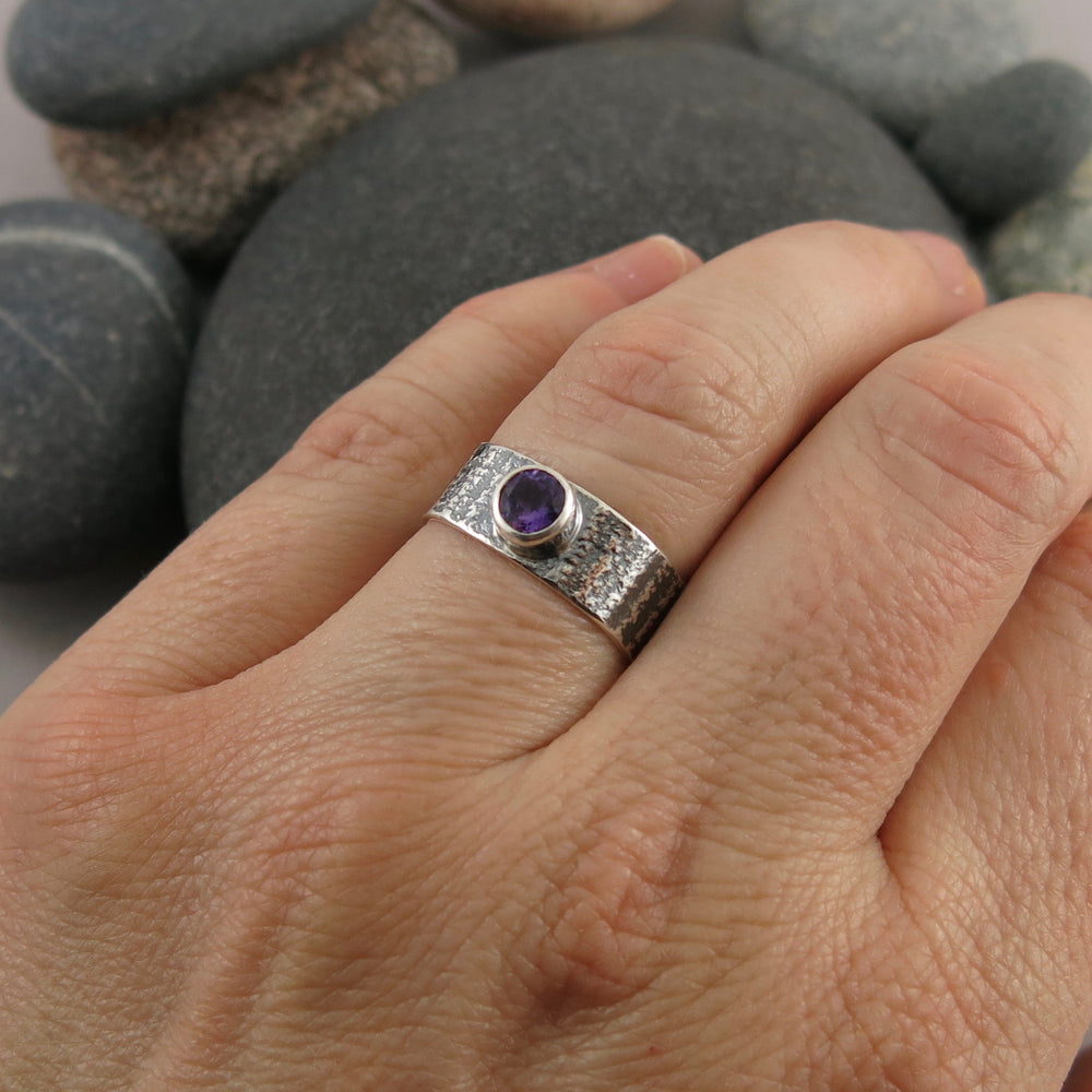 Artisan made jewel drop gemstone ring by Mikel Grant Jewellery. Round faceted amethsyt on a soft square sterling silver band with oxidized tabby striped design.  Displayed on a hand.