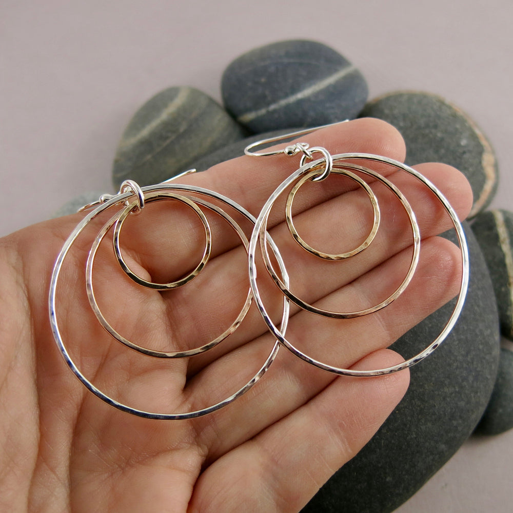 Mixed metal nesting trio circle earrings by Mikel Grant Jewellery. Artisan made hammer textured dangle earrings in silver and gold.  Shown displayed on a hand.