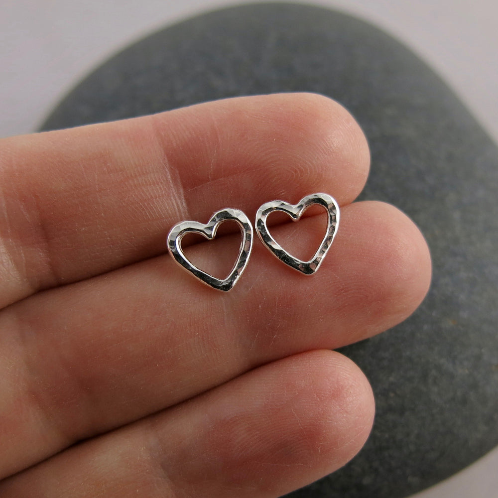 Open heart stud earrings by Mikel Grant Jewellery.  Artisan made hammer textured silver everyday studs.  Shown displayed on a hand.