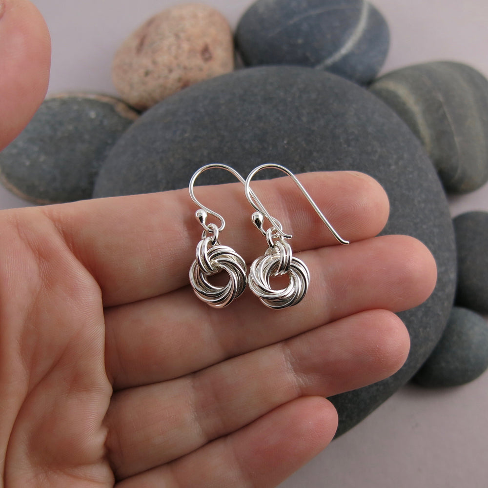 Love knot earrings in sterling silver by Mikel Grant Jewellery. Displayed on a hand.