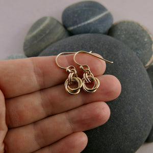 Solid gold love knot earrings by Mikel Grant Jewellery. Artisan made moveable infinite knot earrings.  Show displayed on a hand.